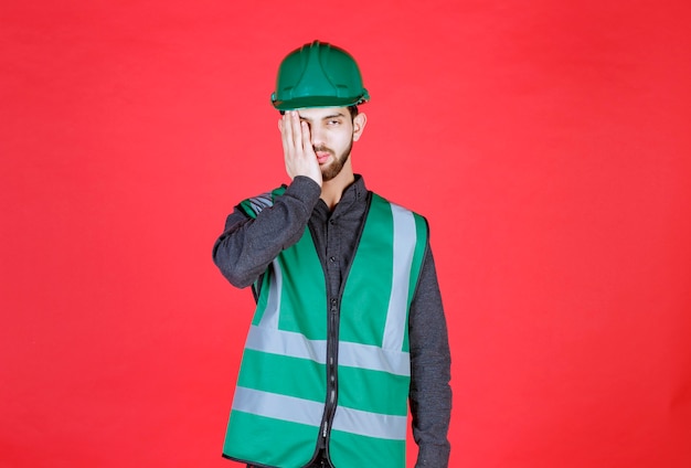 O engenheiro de uniforme verde e capacete parece cansado e com sono.