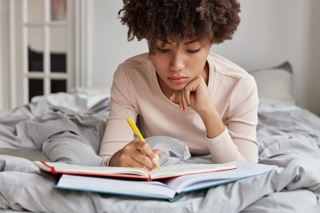 O estudante sério de pele escura se prepara para o exame desde o início da manhã, escreve notas importantes do livro no caderno, deita-se na cama desarrumada no próprio quarto.