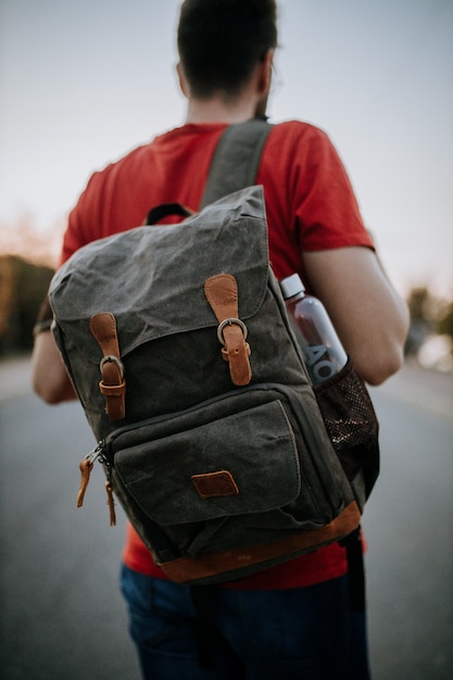 O foco seletivo atirou no homem parado na estrada com uma mochila de aba e uma garrafa de água.