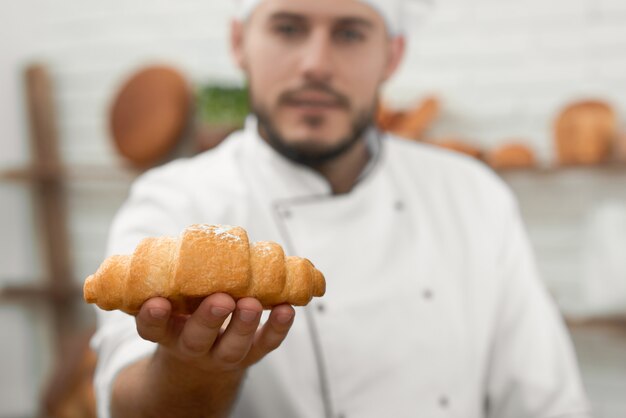 O foco seletivo em um padeiro profissional do croissant saboroso fresco está escondendo o conceito da padaria da loja da loja da disconto da venda do alimento da ocupação da profissão do copyspace.