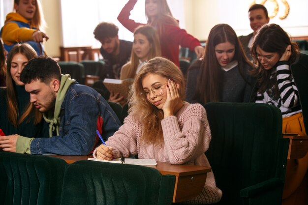 O grupo de estudantes felizes alegres, sentado em uma sala de aula antes da lição