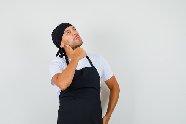 O homem Baker olhando para cima com camiseta, avental e parecendo pensativo