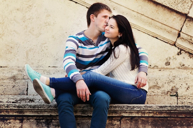 O homem beija a cabeça da mulher sentada diante do muro em Roma