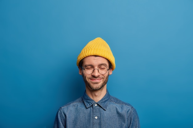 O homem caucalense otimista mantém os olhos fechados, sorri feliz, usa capacete amarelo e camisa jeans