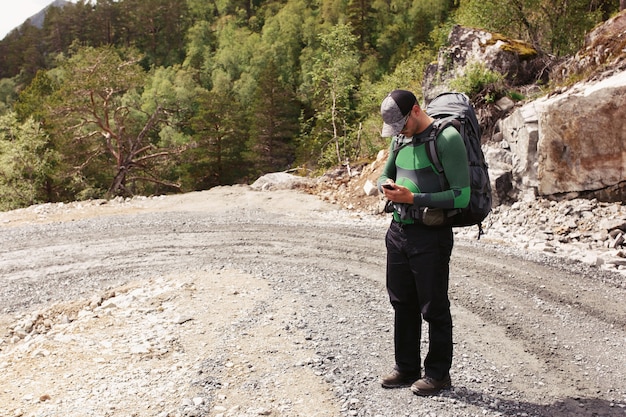 O homem com mochilas verifica seu telefone em pé na estrada