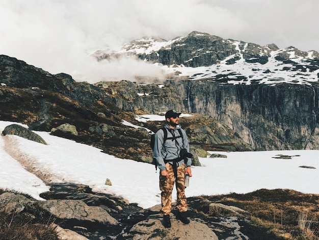 O homem com uma câmera e uma mochila fica diante das montanhas cobertas de neve