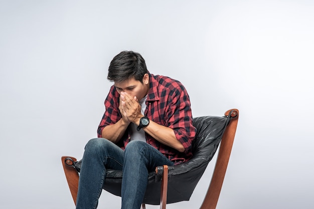 O homem com uma camisa listrada está doente, sentado em uma cadeira e cruza os braços.