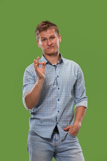 O homem de negócios feliz, assina está bem, sorrindo, isolado no estúdio verde na moda.