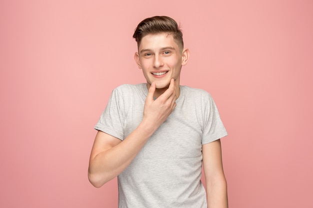 O homem de negócios feliz em pé e sorrindo contra a parede rosa.