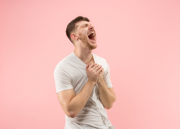 O homem de negócios feliz em pé e sorrindo contra o fundo rosa.