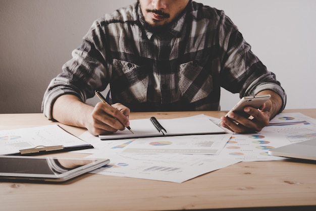 O homem de negócios novo escreve em um caderno ao trabalhar dados de negócio da análise no escritório.