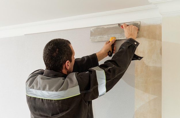 O homem está cortando o papel de parede Reparo de manutenção trabalha renovação no apartamento Ideia de renovação e restauração de apartamento dentro de casa