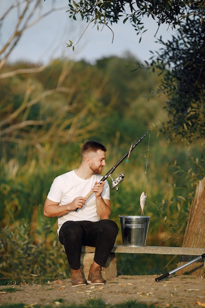 Foto grátis o homem está sentado perto de uma árvore e pescando. pescador olhando um peixe na vara de pescar