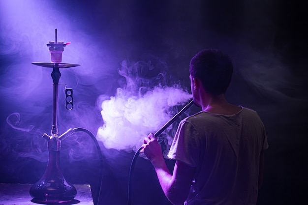 O homem fumando o clássico Shisha. Lindos raios coloridos de luz e fumaça. O conceito de fumar narguilé.