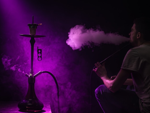 O homem fumando o clássico shisha. lindos raios coloridos de luz e fumaça. o conceito de fumar narguilé.