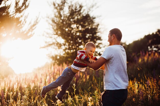 O homem joga seu filho levantando-se no campo com as luzes do sol da tarde