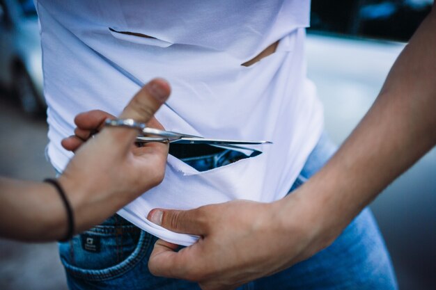 O homem leva as tesouras para cortar a camisa branca