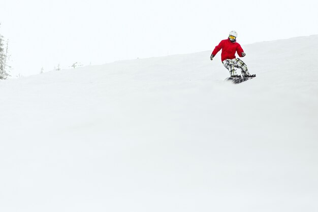 O homem no casaco de esqui vermelho desce a colina no seu snowboard