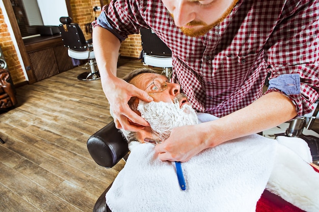 O homem sênior emocionado visitando o cabeleireiro na barbearia