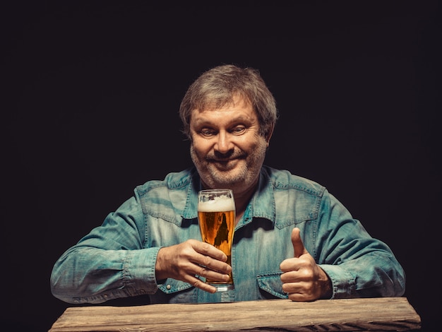 O homem sorridente na camisa jeans com copo de cerveja