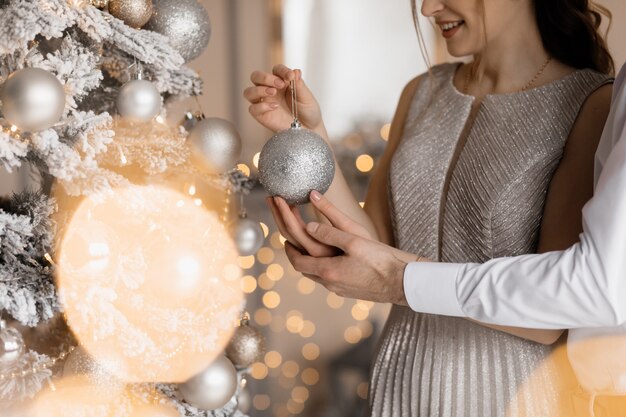 O homem vestido extravagante e a mulher no vestido de prata abraçam-se mutuamente em pé antes de uma árvore de Natal