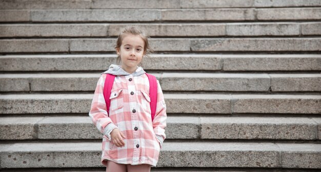 O início das aulas e o primeiro dia do outono. Uma doce menina está de pé contra uma grande escadaria larga.