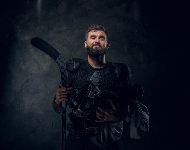 O jogador de hóquei tatuado brutal está posando para o fotógrafo no estúdio fotográfico escuro.