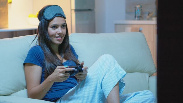 O jogador usando joystick para jogar videogame no console, sentado no sofá da sala. Mulher determinada e animada usando o controle do gamepad, o teclado do playstation, e se divertindo com um jogo eletrônico