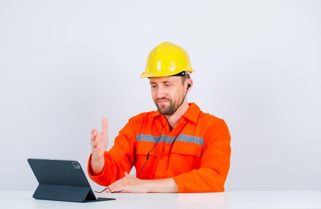 O jovem arquiteto está levantando a mão sentado em frente ao tablet no fundo branco