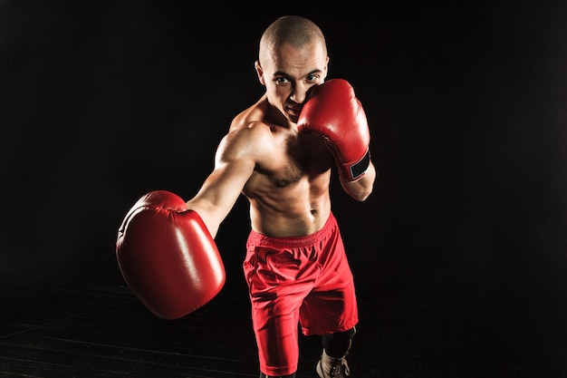 O jovem atleta masculino de kickboxing em um fundo preto
