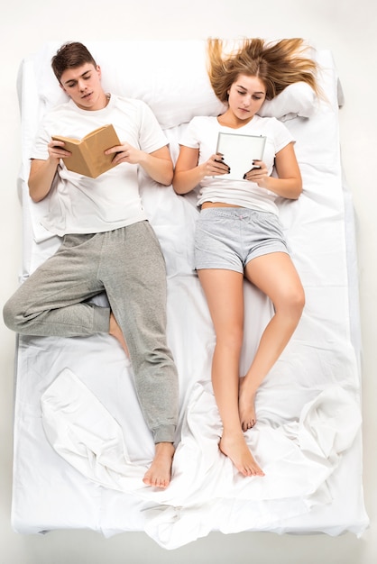 O jovem casal adorável, deitado em uma cama com livros