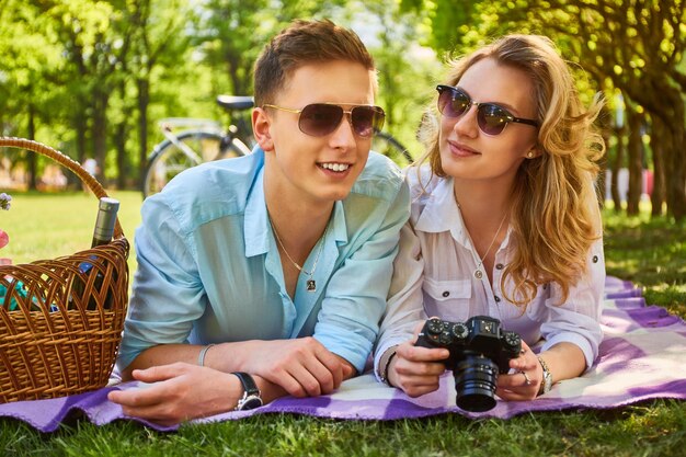 O jovem casal atraente usando uma câmera fotográfica compacta em um piquenique em um parque.