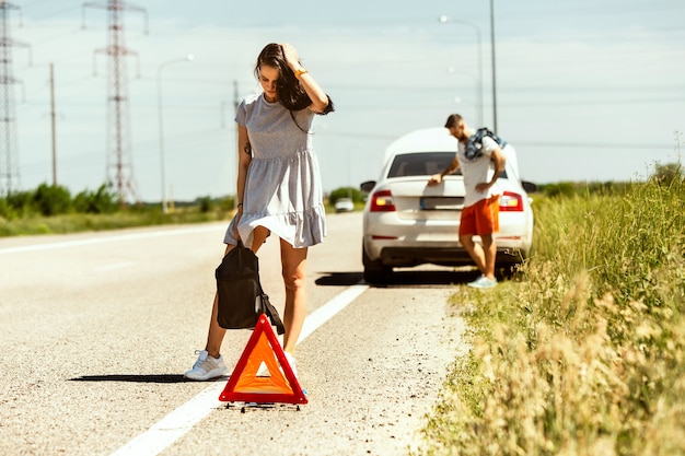 O jovem casal quebrou o carro durante uma viagem para descansar. Eles estão tentando parar outros motoristas e pedir ajuda ou pedir carona