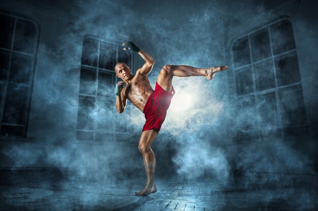 O jovem fazendo kickboxing na fumaça azul