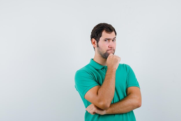 O jovem irritado está pensando segurando a mão na mandíbula no fundo branco