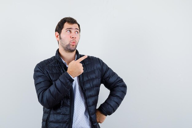 O jovem pensante está apontando para a direita com o dedo indicador no fundo branco