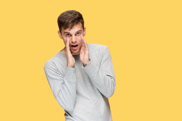 O jovem sério olhando com cautela no estúdio amarelo e falando em segredo para a câmera