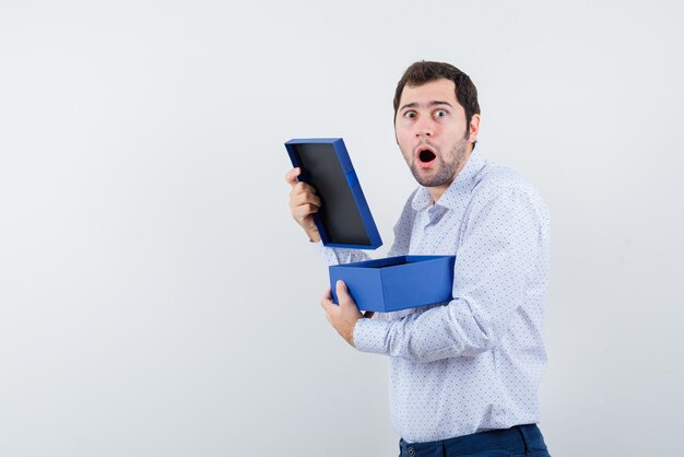 O jovem surpreso segurando a caixa azul no fundo branco