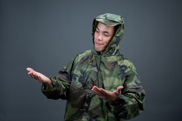 O jovem usa uma capa de chuva de camuflagem e mostra diferentes gestos.