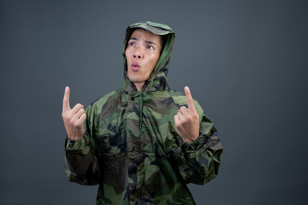 O jovem usa uma capa de chuva de camuflagem e mostra diferentes gestos.