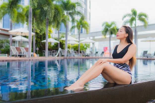 O lazer asiático novo bonito da mulher do retrato relaxa o sorriso em torno da piscina exterior para férias