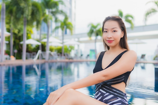 O lazer asiático novo bonito da mulher do retrato relaxa o sorriso em torno da piscina exterior para férias