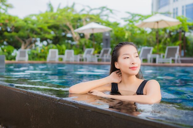 O lazer asiático novo bonito da mulher do retrato relaxa o sorriso em torno da piscina exterior para férias