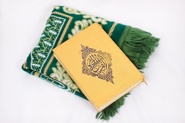 O livro sagrado al quran e tapete de oração isolado no fundo branco
