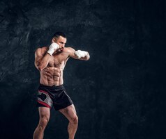 O lutador musculoso forte está mostrando seu soco enquanto posava para o fotógrafo no estúdio fotográfico escuro.