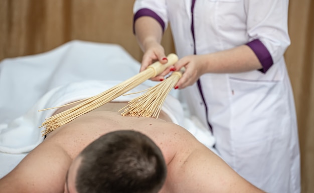 O massagista faz uma massagem japonesa em um homem com vassouras de bambu.