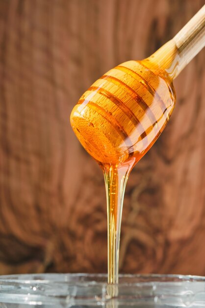 O mel flui de um bastão de mel de madeira para uma jarra Fechamento de tiro vertical e foco seletivo no fundo de laje natural de mel Produtos naturais de fazendas na Turquia