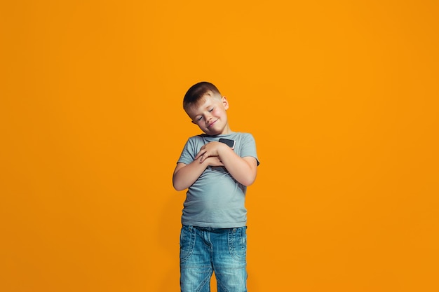 Foto grátis o menino adolescente feliz em pé e sorrindo contra um fundo laranja.