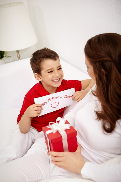 O menino de sorriso com um presente para sua mãe