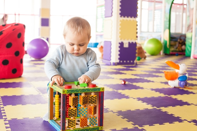 O menino de um ano de idade brinca com um cubo de habilidades motoras finas na sala de jogos